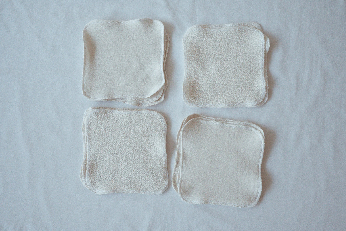 Four organic cotton washcloths from cabane childrenswear are arranged in a 2x2 grid on a white surface. Named the "Organic Washcloth Set of 4," these undyed, neatly sewn fabric squares feature soft textures that vary slightly on each side to ensure a gentle washing experience.