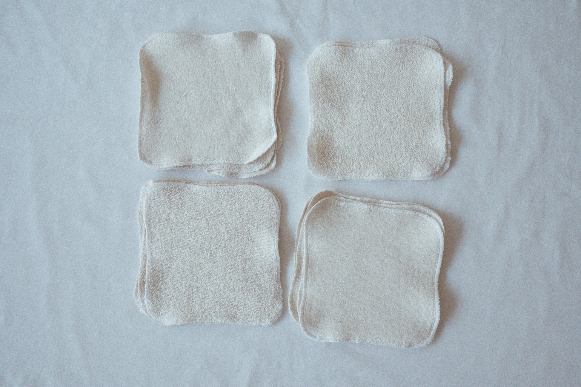 Four organic cotton washcloths from cabane childrenswear are arranged in a 2x2 grid on a white surface. Named the "Organic Washcloth Set of 4," these undyed, neatly sewn fabric squares feature soft textures that vary slightly on each side to ensure a gentle washing experience.