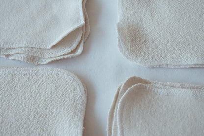 A set of four stacked Organic Washcloths from cabane childrenswear displayed on a light surface, organized into neat piles. Each washcloth features precisely serged edges. The image highlights the soft texture and simplicity of undyed organic cotton, promising a gentle washing experience.