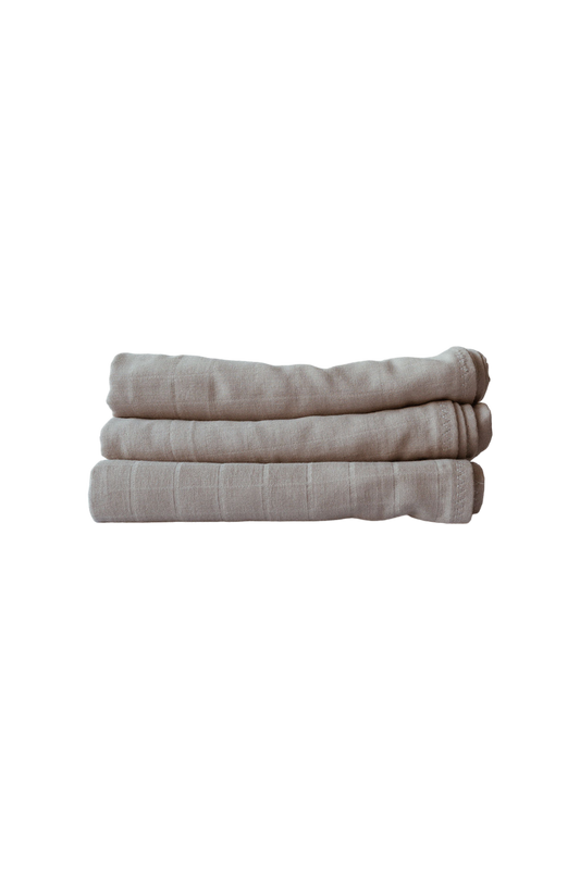 A neatly folded stack of three light beige, lightweight ORGANIC COTTON SQUARE towels in the color mushroom, from cabane childrenswear, placed against a white background. Handmade in Vancouver, these towels feature a subtle striped texture that adds a hint of detail.