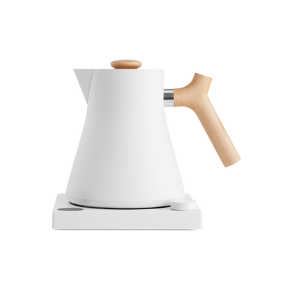 The Corvo EKG Electric Kettle by Fellow Wholesale showcases a sleek, modern design with a white matte finish, complemented by a wooden handle and lid knob. It rests on a matching white base with a small circular control button, and features variable temperature control along with quick heat time. The kettle's minimalistic style and clean lines contribute to its contemporary aesthetic.