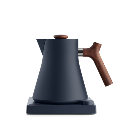 The Corvo EKG Electric Kettle by Fellow Wholesale is a sleek, matte black appliance featuring a wooden handle and knob, positioned elegantly on its matching base. Precision engineered with a modern, minimalist design, it showcases clean lines and a smooth surface. The base is equipped with a variable temperature control dial located on the front-right corner.