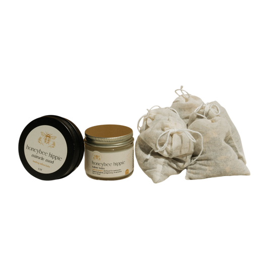 Two Honeybee Hippie jars labeled "miracle mud" and "pure honey mask," featuring beige lids, and a pile of small tied mesh bags exude natural elegance against a black background in the Natural Mama Bundle.