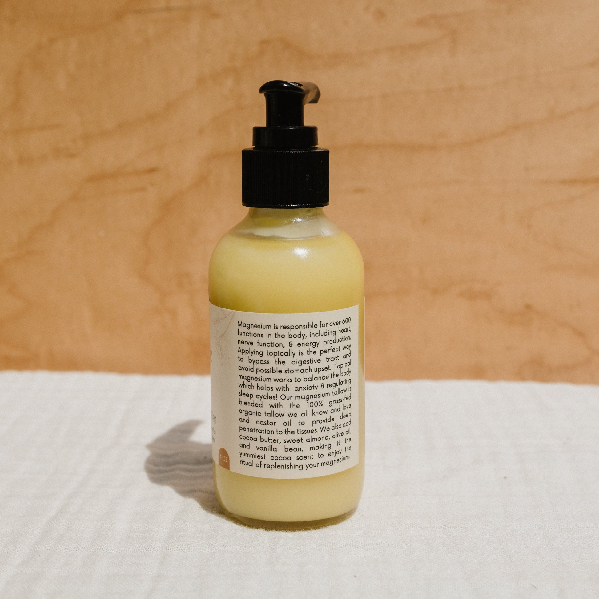 A bottle of Honeybee Hippie's yellow magnesium butter lotion with a black pump sits on a soft white surface against a tan background, featuring a label in small text that promises stress relief for better sleep.