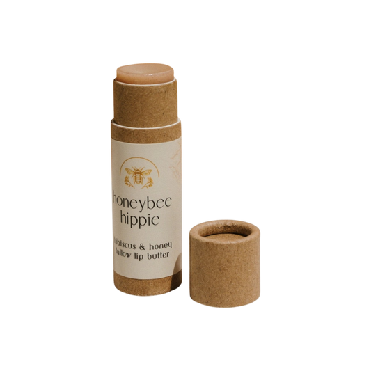 A cardboard tube of Honeybee Hippie's hibiscus & honey tallow lip butter offers delightful flavors with the cap beside it, showcasing the top of this nourishing product made with organic herbs.