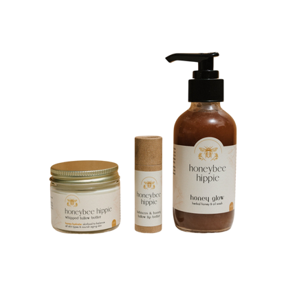 The Honeybee Hippie's "The Honey Bundle" includes a whipped kokum butter jar, kokum and honey balm stick, and herbal honey shower gel pump—all with natural ingredients for skin health, featuring cream-colored labels with minimalist design on a black background.