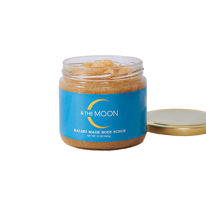 A transparent jar contains the Malibu Made Body Scrub, a light brown blend of natural vanilla brown sugar and organic oils. The blue label reads "C & The Moon." The lid is off and placed next to the jar, revealing its 12 oz (340g) contents.