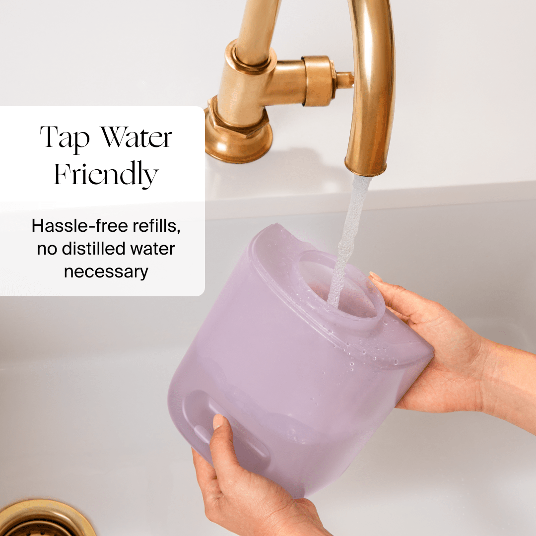 Someone fills a Canopy Bedside Humidifier 2.0 in purple with tap water from a gold faucet. The text on the image says, "Tap Water Friendly. Hassle-free refills, no distilled water necessary." Enjoy convenience with every use—fulfilled by Canopy.