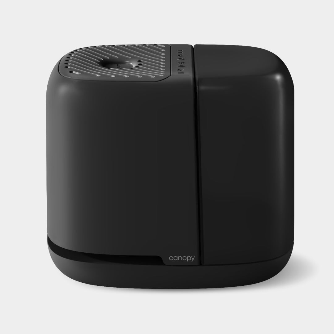 A sleek, modern black humidifier in a smooth, rounded rectangular shape with a perforated top surface, the Bedside Humidifier 2.0 by Canopy features a minimalist design and small "canopy" logo at the base, ensuring quality fulfillment by Canopy.