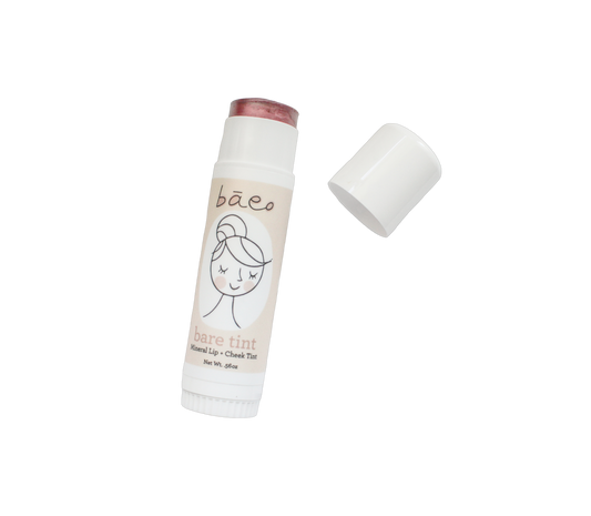 A tube of bāeo bare tint lip and cheek tint with its cap removed, showcasing the pinkish-red balm tip. The beige cylindrical container features a minimalistic illustrated face design, promising a natural finish and hydration against a plain black background.