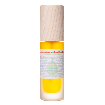 A small cylindrical bottle with a wooden cap, containing a yellow liquid labeled "Best Skin Ever Cleanser - Seabuckthorn" by Living Libations. The label includes detailed text about the product's use as a cleanser and moisturizer, enriched with organic oils and botanical compounds.