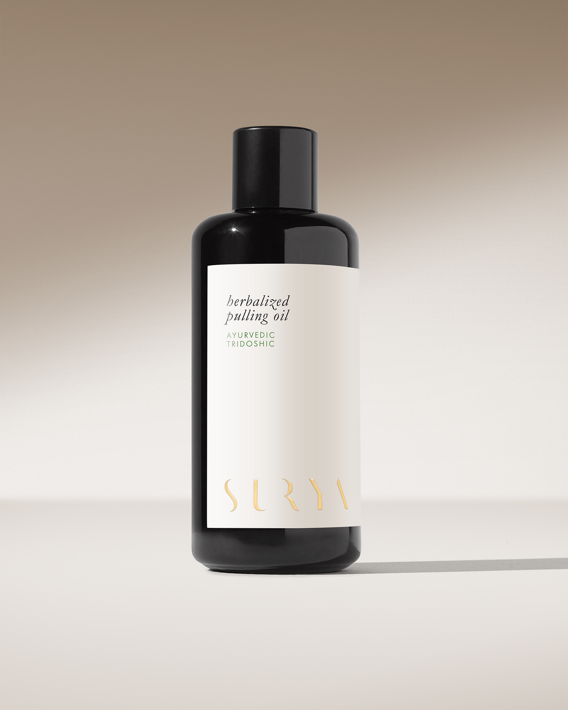 A sleek black bottle with a minimalistic white label stands against a neutral background. The label reads "Herbalized Pulling Oil, Ayurvedic Tridoshic" in simple text. At the bottom, the brand name "Surya" is elegantly printed in gold lettering, honoring the ancient practice of Ayurveda.