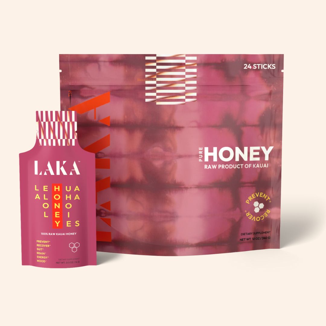 The image showcases a pink and maroon package labeled "Honey" with the text "Raw Product of Kauai." The package contains 24 LAKA Honey Sticks™. One stick is placed in front, promoting raw honey for immune support, and is labeled "LAKA" with white and yellow text along with a decorative pattern.