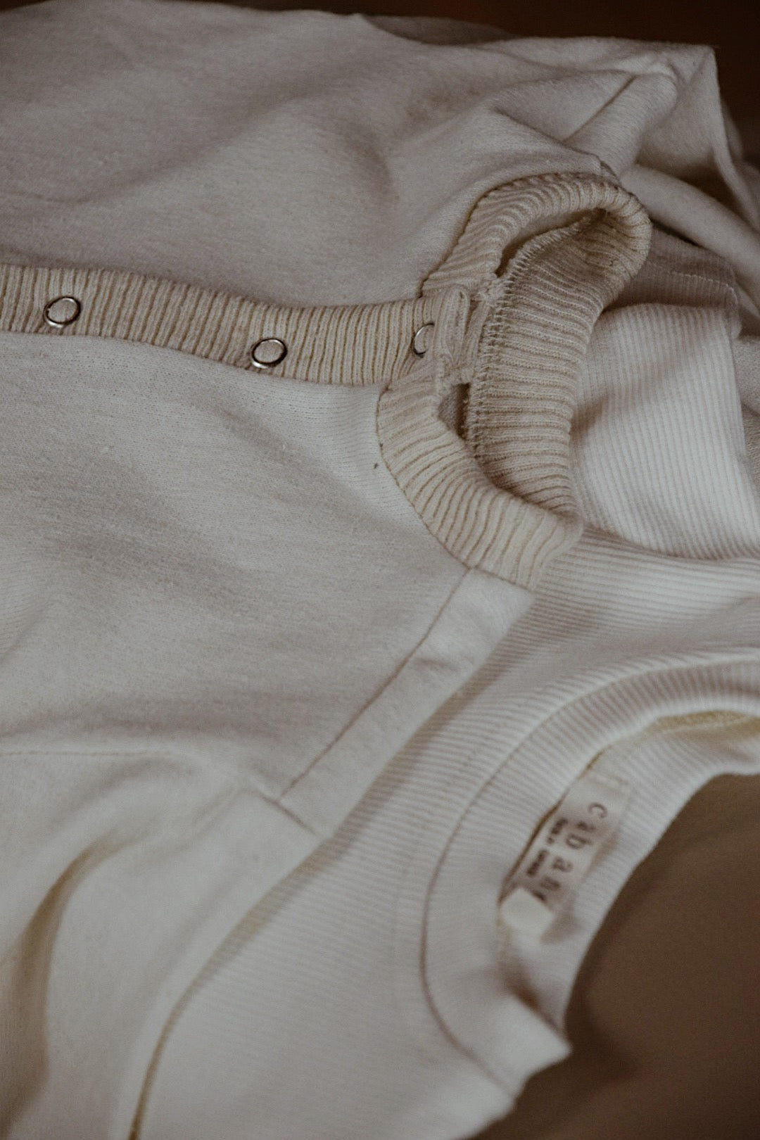 Image Description: A close-up image showcasing a neatly folded, ethically handmade white ribbed knit Soul Sweater Baby + Kid cardigan with metallic snap buttons, placed atop a white ribbed knit t-shirt. These garments from cabane childrenswear are crafted from organic cotton and hemp, exuding a soft and comfortable fabric.