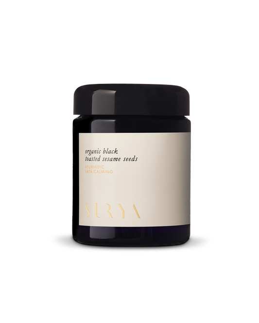 A black jar with a cream-colored label displays the text "Organic Black Sesame Seeds" and "VATA CALMING, AYURVEDIC, SURYA." Packed with antioxidants and protein, the round jar features a sleek black lid.