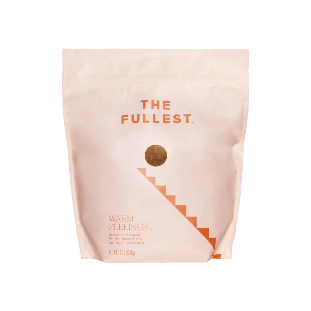 A light peach-colored, resealable bag with "THE FULLEST" written at the top in bold orange letters. Below, a gold circle leads to a staircase graphic. The bottom of the bag reads "Warm Feelings Bulk," indicating it is a caffeine-free saffron latte powder dietary supplement designed to improve mood.