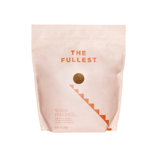 A light peach-colored, resealable bag with "THE FULLEST" written at the top in bold orange letters. Below, a gold circle leads to a staircase graphic. The bottom of the bag reads "Warm Feelings Bulk," indicating it is a caffeine-free saffron latte powder dietary supplement designed to improve mood.