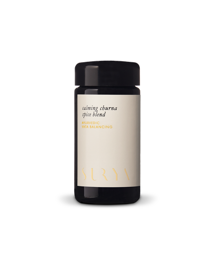 A black cylindrical container with a light beige label that reads "Calming Digestive Spice Blend" and "AYURVEDIC VATA BALANCING." Featuring organic ingredients, the brand name "Surya" is placed at the bottom of the label in a minimalist font. Perfect for cooking dahl.