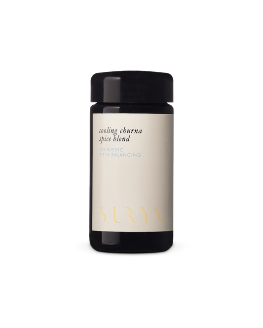 A dark glass jar labeled "Cooling Digestive Spice Blend" proudly bears the brand name "Surya," with its minimalist design and cream-colored label elegantly conveying a sense of tranquility and wellness.