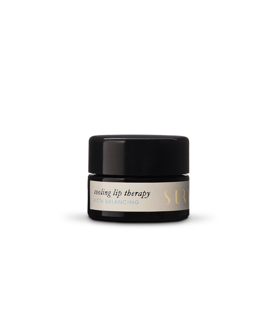 A small black cylindrical container of Cooling Lip Therapy, labeled "Pitta Balancing" in gold and white text on a light-colored background, with the brand name "Surya" partially visible. This lip balm features natural blends creating an organic ingredient base for soothing relief.