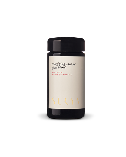 A dark-colored jar with a black lid containing "Energizing Digestive Spice Blend" from the esteemed brand Surya, featuring the label text "Ayurvedic Kapha Balancing." Made with organic ingredients, the jar is set against a gradient background.