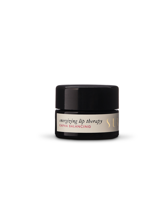 A small black jar featuring a white label with the text "Energizing Lip Therapy - Kapha Balancing" by Surya. The natural lip therapy is packaged in a jar with a black lid and gold embossed text on the label, set against a neutral background.