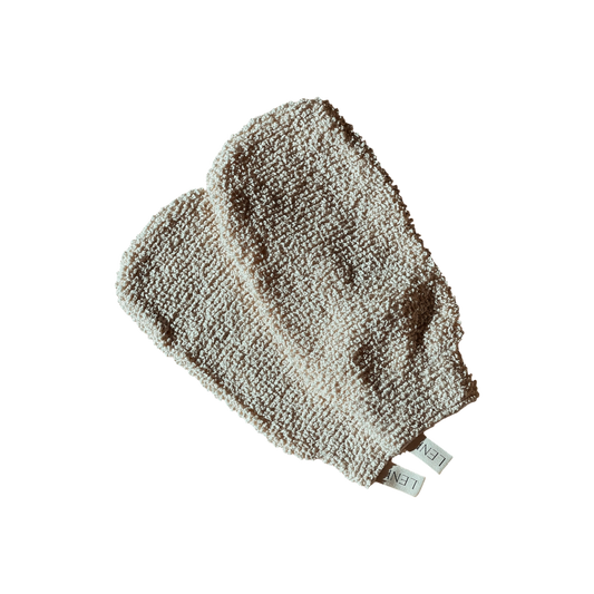 A pair of cream-colored, textured exfoliating mitts featuring small fabric tags labeled "LENI." Known as The Scrub Mitts, they are ideal for dry scrubbing. The mitts are showcased against a black background.