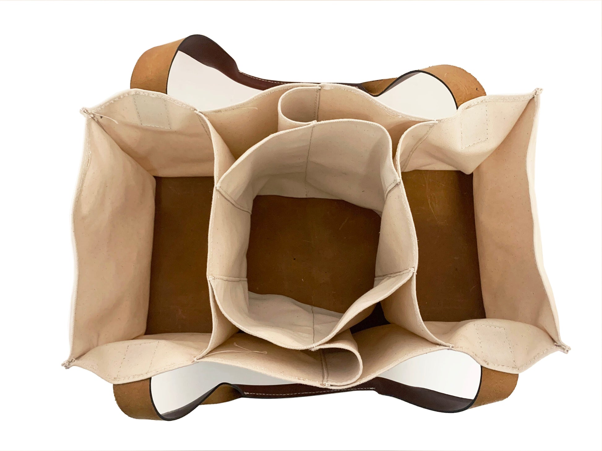 A beige, multi-pocketed canvas Market Sac from Agnes Baddoo with dark brown leather handles is viewed from above. This bag features a large central compartment surrounded by multiple smaller pockets, providing organized storage spaces. The inside of the leather and canvas bag is lined with light fabric.