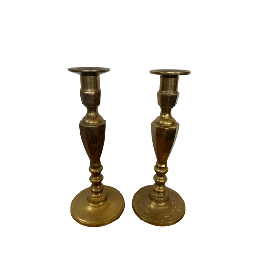 Displayed against a black background, the Vintage Brass Candle Holders from Shoppe Maison showcase exquisite ornate detailing on their bases and stems, with a polished, reflective surface.