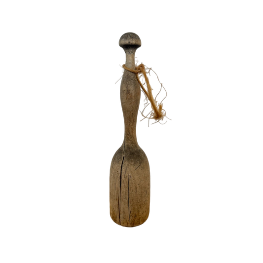 A vintage wood masher with a rounded handle and a flat, slightly cracked base, wrapped with twine around the neck, is set against a plain black background. Discover this charming piece at Shoppe Maison, where vintage homewares come to life.