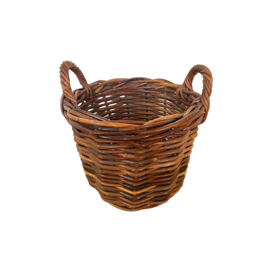 The Vintage Woven Basket with Handles from Shoppe Maison is a round, slightly tapered basket made of natural brown rattan. It features two looped handles on either side and boasts a tight, uniform weave.