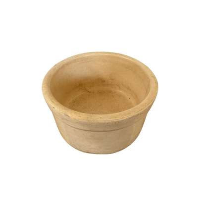 A round, beige ceramic bowl with a slightly textured surface and a smooth rim, reminiscent of vintage stoneware crock pieces. The Vintage Small Stoneware Crock by Shoppe Maison is empty and placed against a plain, black background, perfect for showcasing their curated collection of vintage goods.