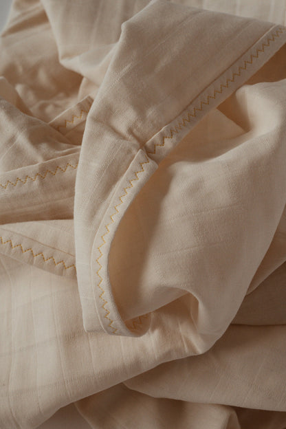 Close-up of the Organic Cotton Cover, Undyed by cabane childrenswear, showcasing its naturally beige fabric with a folded edge and zigzag stitching along the border. The cotton square material looks soft and textured, forming gentle folds and shadows that highlight its handmade craftsmanship in Vancouver.