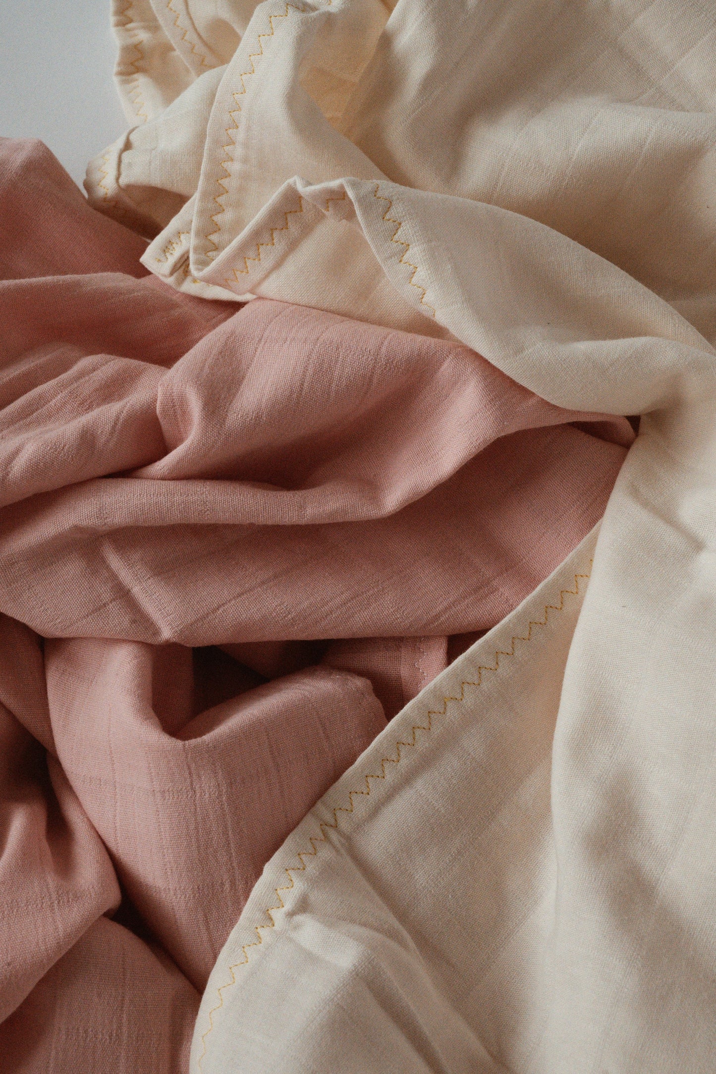 Close-up of the Organic Cotton Cover by cabane childrenswear, featuring soft, crumpled fabric in cream and dusty pink colors. This undyed cover showcases visible zigzag stitching along its edges, highlighting its smooth and delicate texture.