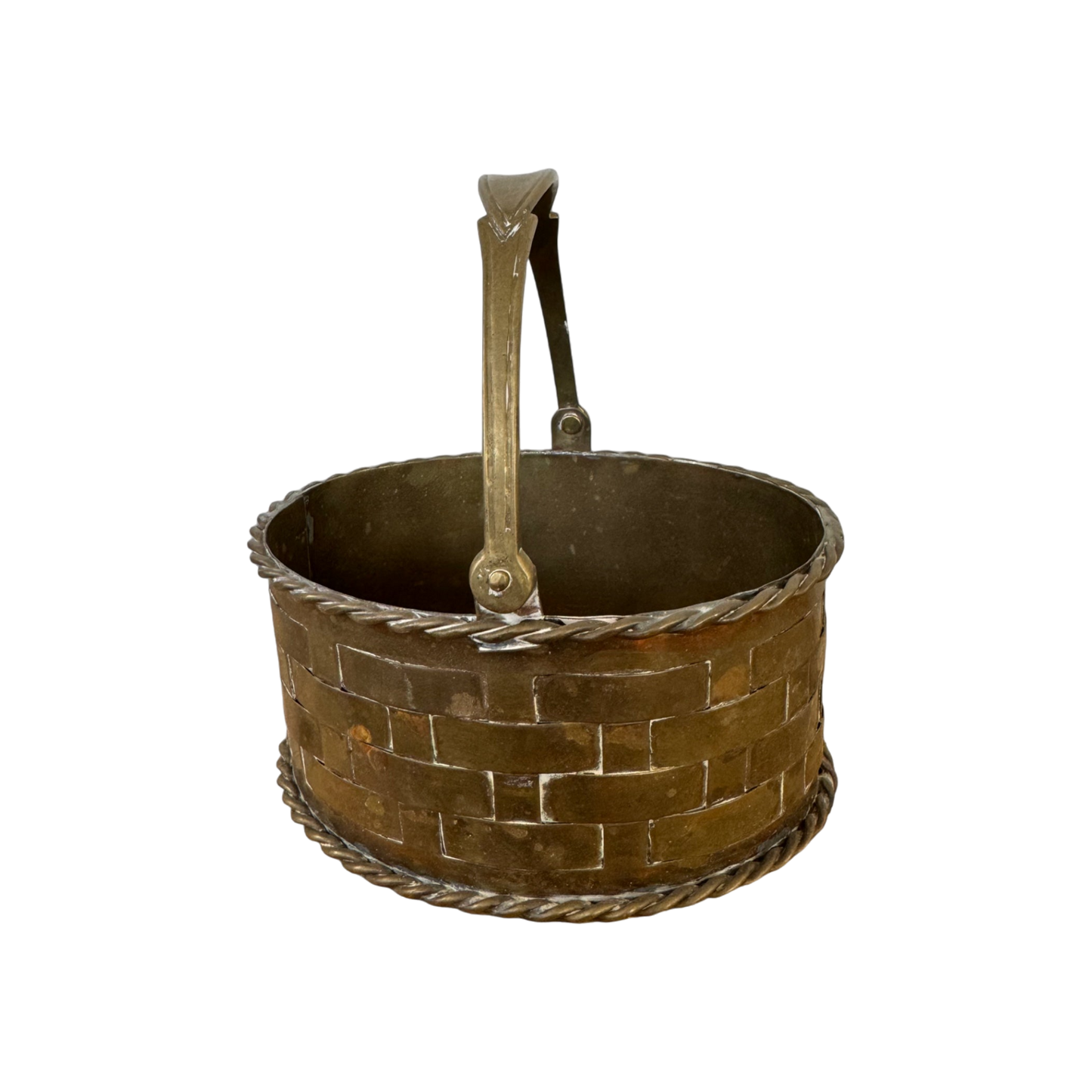 The Mini Brass Basket by Shoppe Maison is a rustic, round metal basket featuring a woven lattice pattern and a handle. This vintage piece is designed from brass and showcases twisted rope-like details along the base and top rim, all set against a solid black background.