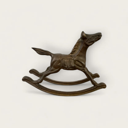 The Brass Rocking Horse by Shoppe Maison is depicted in this bronze sculpture, reminiscent of a traditional toy. Mounted on a curved base, it captures the essence of vintage goods. Set against a plain white background, the piece emphasizes its detailed craftsmanship and elegant form—truly a Shoppe Maison treasure.