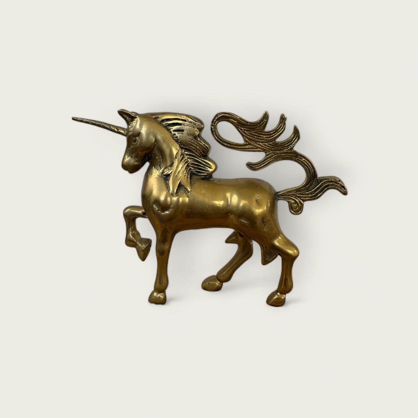 A Mini Brass Unicorn from Shoppe Maison, elegantly crafted with a polished finish and standing on three legs with one front leg raised. Its flowing mane and tail add to its allure, while a long, straight horn graces its forehead. Perfect for lovers of vintage goods, this charming piece stands out beautifully against a plain white background.