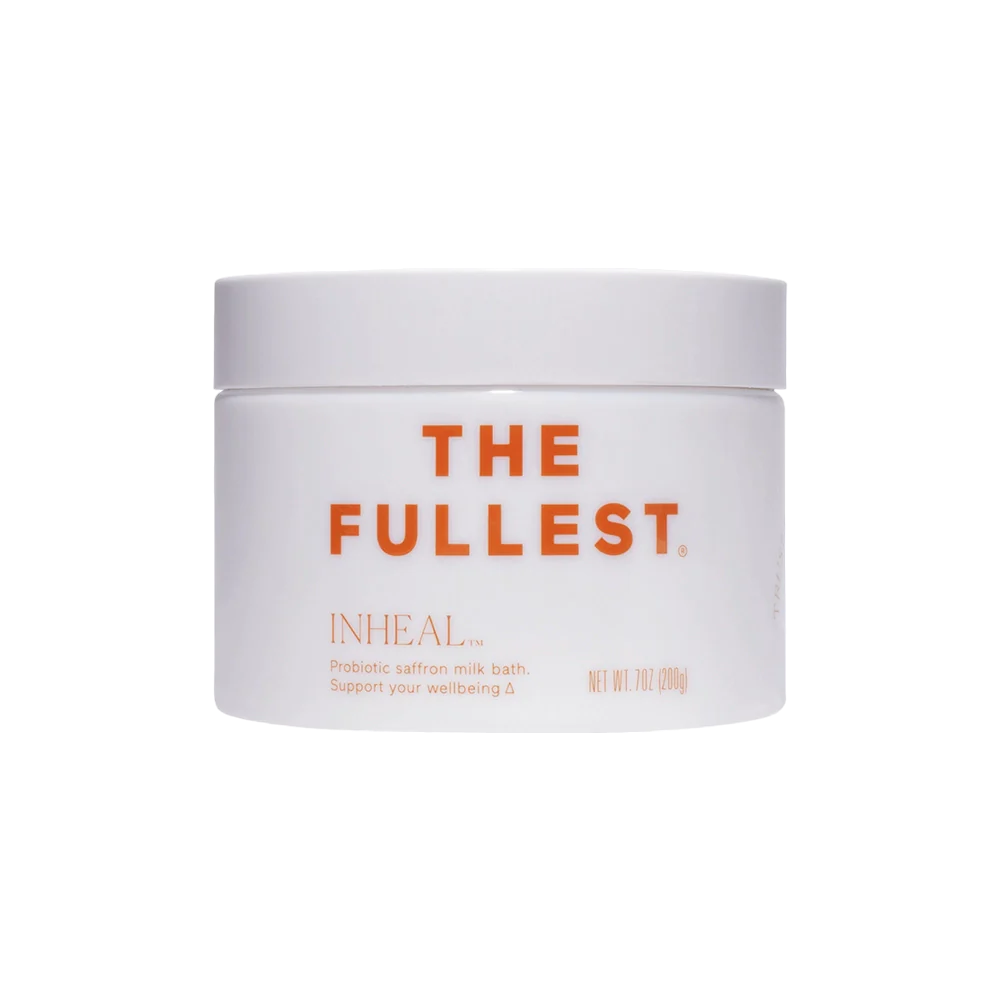 A white, circular container labeled "THE FULLEST" in orange text on the front displays the product name "Inheal Milk Bath." Below this, there's a description that reads, "Probiotic saffron milk bath. Support your wellbeing and skin hydration." This container is clearly designed for bath use.