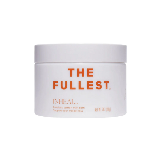 A white, circular container labeled "THE FULLEST" in orange text on the front displays the product name "Inheal Milk Bath." Below this, there's a description that reads, "Probiotic saffron milk bath. Support your wellbeing and skin hydration." This container is clearly designed for bath use.