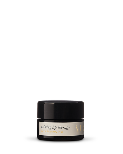 A small, black cylindrical jar labeled "Calming Lip Therapy - Vata Balancing" from the brand Surya. The jar features a black lid and an off-white label with subtle text. The product, with a creamy formula and organic ingredients, is designed for moisturizing lip care.