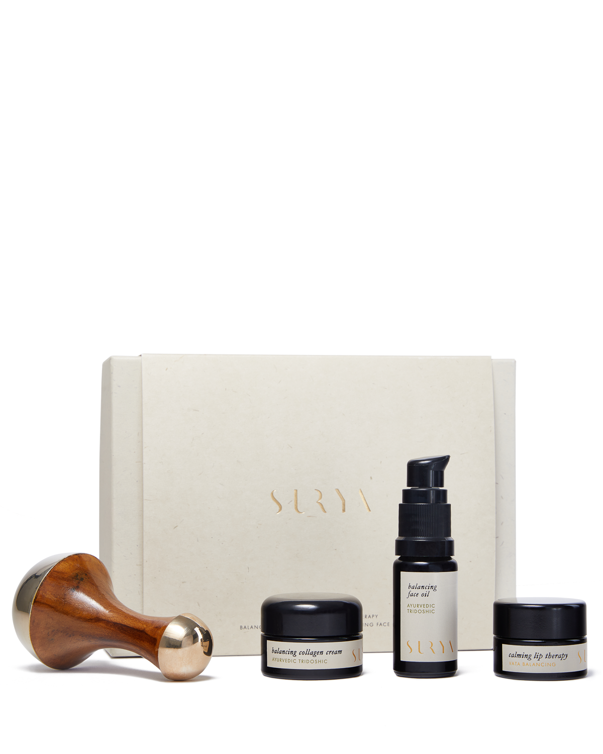 The image showcases the Surya Skincare Discovery Set, featuring a wooden-handled Kansa Wand, a jar labeled "balancing collagen cream," a bottle labeled "balancing face serum," and a jar labeled "nourishing lip therapy," all elegantly arranged in front of a beige Surya box.