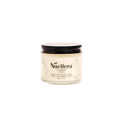 A 56-gram (2-ounce) glass jar of Nucifera Body Store's The Balm with a black screw-on lid. The label, adorned with minimalist line-drawn leaves, describes the product as a vegan unisex skincare essential, perfect for enhancing skin tone and texture.