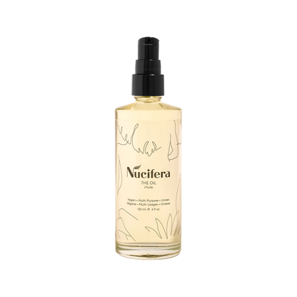 A clear bottle of Nucifera Body Store's The Oil, a multi-purpose vegan oil with a black pump top. The minimalist design features abstract line drawings and black text that reads "Nucifera The Oil." This 120 ml (4 fl oz) bottle promises to deliver a radiant glow.