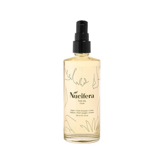 A clear bottle of Nucifera Body Store's The Oil, a multi-purpose vegan oil with a black pump top. The minimalist design features abstract line drawings and black text that reads "Nucifera The Oil." This 120 ml (4 fl oz) bottle promises to deliver a radiant glow.