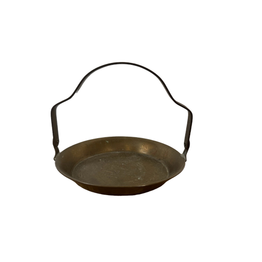 Introducing the Mini Brass Tray by Shoppe Maison: A round, bronze-colored metal tray with a flat bottom and slightly raised sides. This vintage-inspired piece features a curved metal handle on opposite sides, ideal for carrying or hanging. Set against a black background, it stands out prominently and doubles as an elegant piece of home decor.
