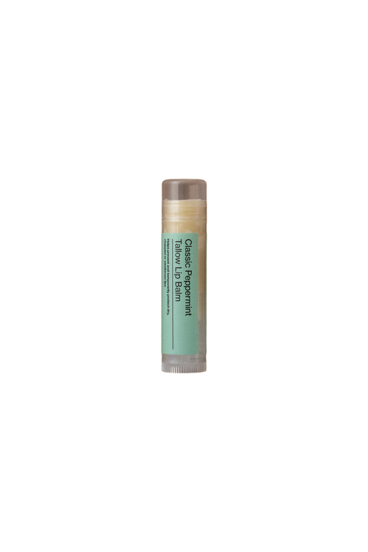 A close-up of a tube of Classic Peppermint Lip Balm - Regenerative Tallow® by Summer Solace Tallow, featuring a blue-green label. The text on the label includes "Classic Peppermint Lip Balm - Regenerative Tallow®" and some smaller, less clear text. Perfect for multipurpose use, this lip balm is housed in a transparent container and delivers a cooling and refreshing sensation.