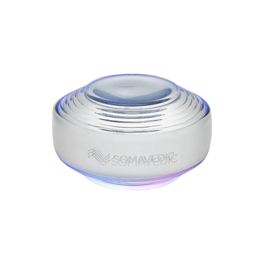 A round, metallic device with a smooth, dome-shaped top and a series of concentric rings. The bottom emits a soft, glowing light. The word "Somavedic USA Sky" is inscribed on the side, promising improved concentration and elevated sleep quality.