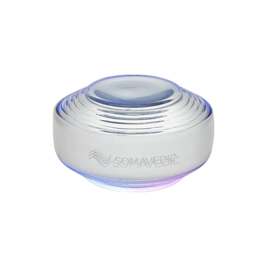 A round, metallic device with a smooth, dome-shaped top and a series of concentric rings. The bottom emits a soft, glowing light. The word "Somavedic USA Sky" is inscribed on the side, promising improved concentration and elevated sleep quality.