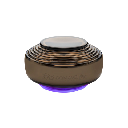 Anthracite-colored, dome-shaped electronic device with multiple concentric ridges, a smooth top surface, and a faint purple glow at its base. Designed to mitigate electromagnetic fields (EMF), the brand name "Somavedic USA" is subtly engraved on its side.