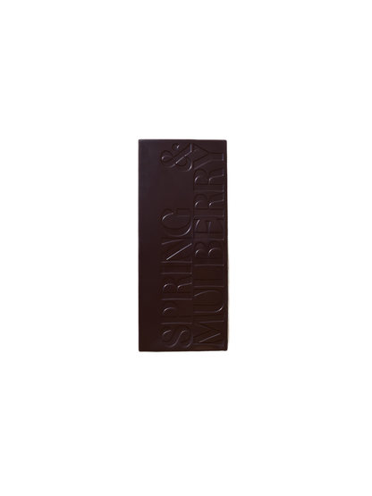 A Pure Dark Date-Sweetened Chocolate bar from Spring & Mulberry, with "SPRING & MULBERRY" engraved in large, bold letters vertically aligned on its surface against a plain black background.